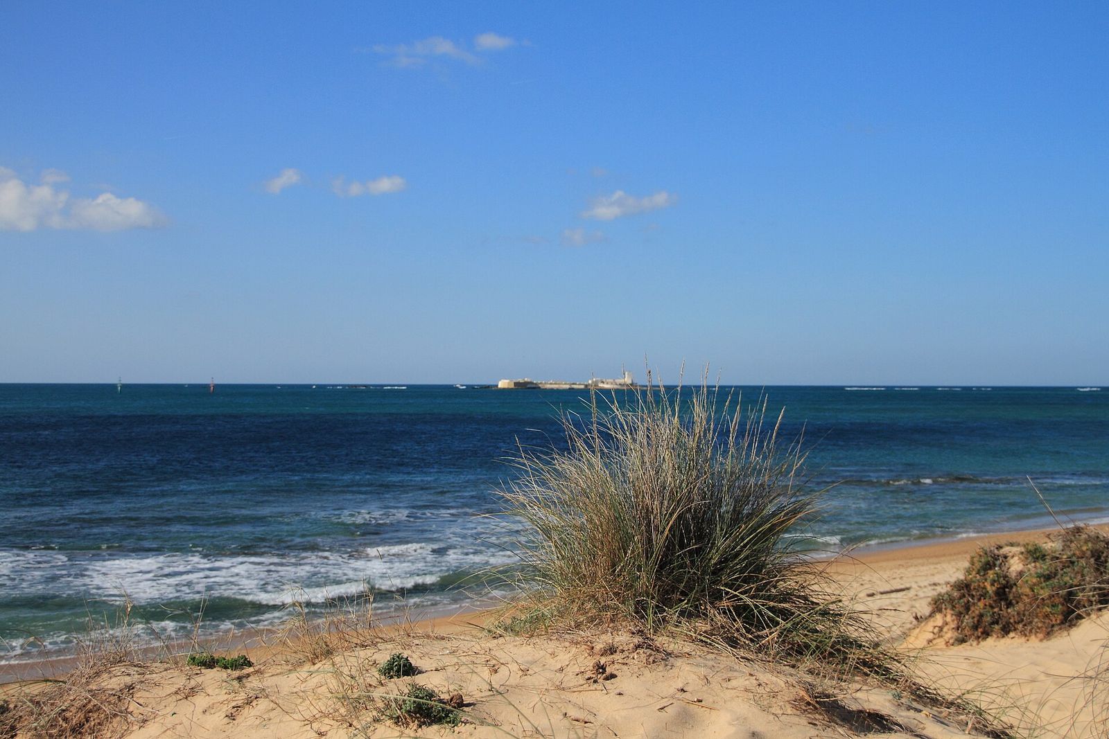 Duna con barrón, mar azul y el castillo de Sancti Petri al fondo, en la playa de Chiclana, sin gente