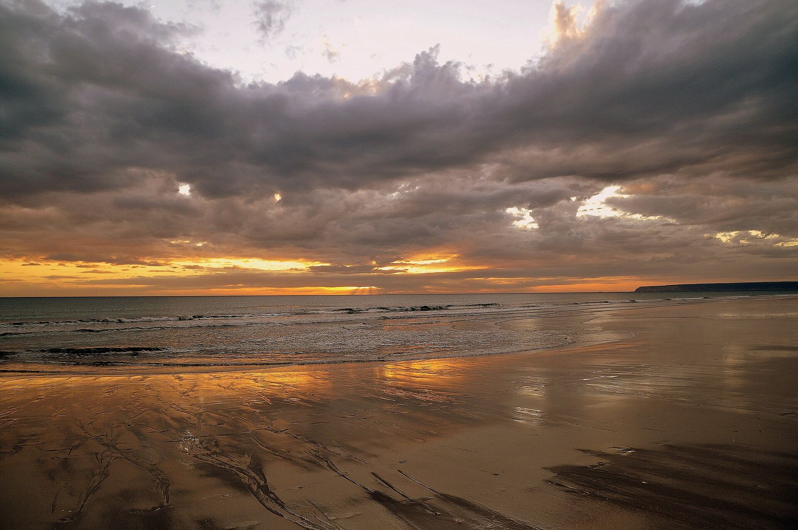 La playa de Zahara de los Atunes vacía al atardecer, con la marea baja reflejando el cielo naranja
